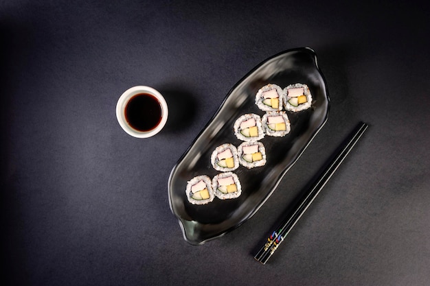 Uramaki with cucumber mango fruit and crab sticks on black plate in a black background Top view