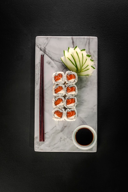 Uramaki-zalm op marmeren plaat met sojasaus en eetstokjes op een zwarte achtergrond. Bovenaanzicht.