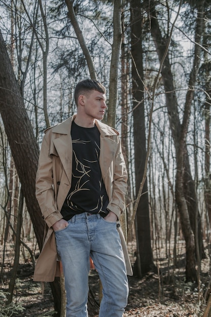 Urban citizen standing in the forest in the beige trench coat and jeans.