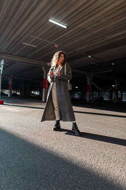 Urban fashion pretty curly woman in vintage long coat with stylish bag walks in the city. Female casual style and beauty