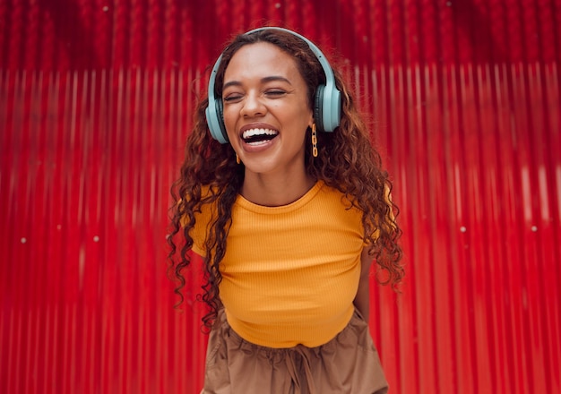 Urban joy and woman with headphone music enjoying happy rhythm with bluetooth connection smile of latino girl listening to feel good streaming audio while resting at wall for leisure break