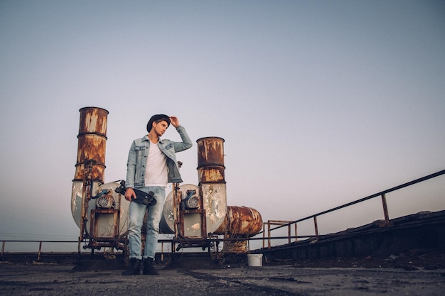 Urban man with hat and skateboard on background of old rusty pipes