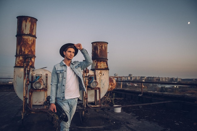 Urban man with hat and skateboard on background of old rusty pipes