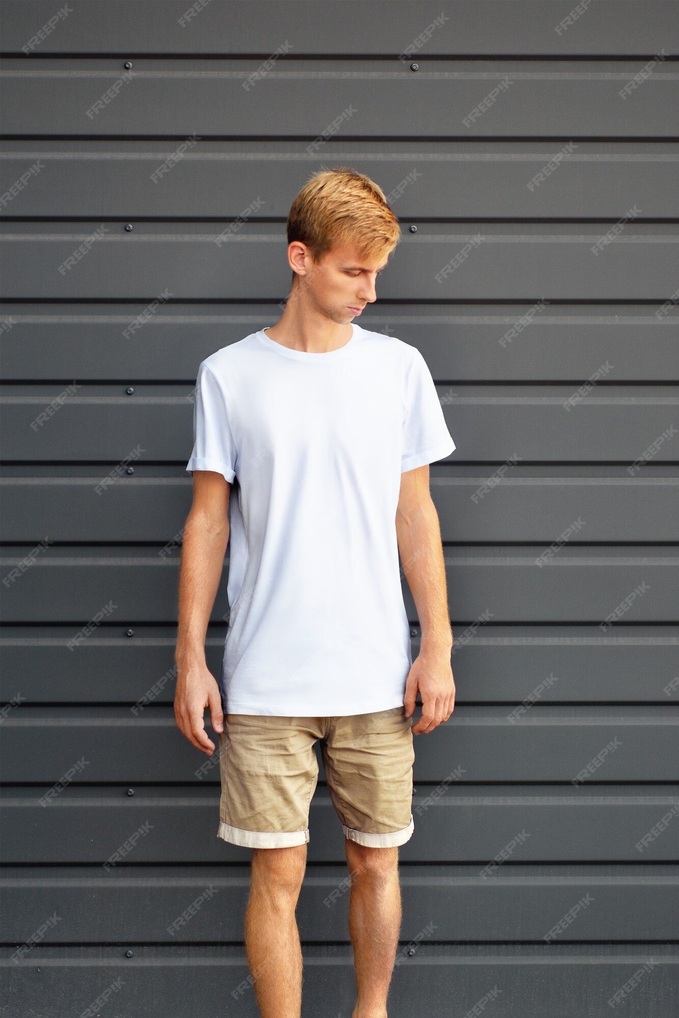 Premium Photo | Urban mockup of clothes. young man standing near the gray  metal profiled wall in a white t-shirt and brown shorts. template can use  for you design.