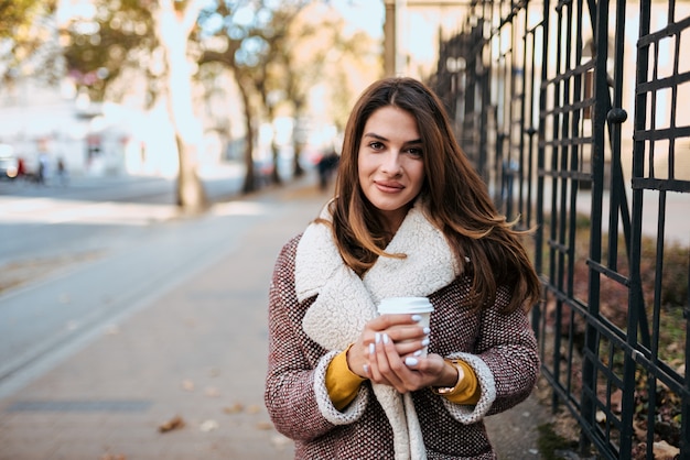 Urban portrait of stylish brunette holding take away coffee.