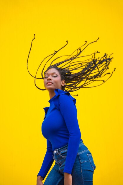 Urban session young darkskinned woman with long braids in a blue dress on a yellow background with a serious look and her braids up