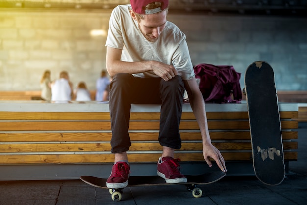 urban street portrait of young hipster sit on the bench with skateboard outdoors.