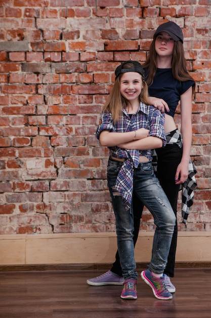 Stile urbano. l'amicizia nell'hip hop. adolescenti femminili alla moda in studio, felicità nel ballo, fondo del muro di mattoni con spazio libero. felice vita di strada, concetto di belle sorelle