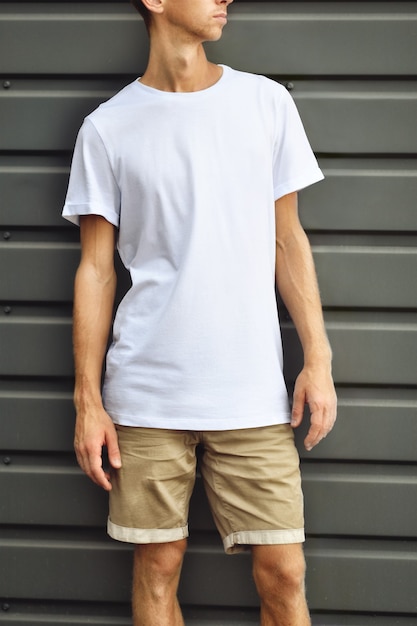 Urban template of clothes. Stylish  guy  standing  near the gray  metal profiled wall in a blank T-shirt and brown shorts.  Mockup ready for you design.