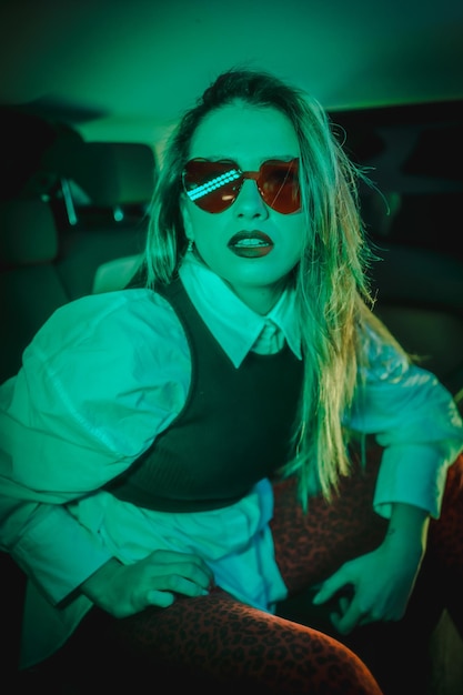 Urban with green neons in the back of a car of a young blond woman with heart glasses