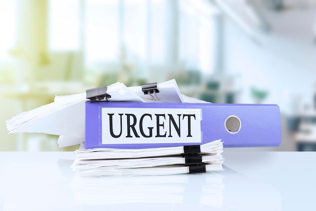 Urgent, deadline, written on document folder in trendy purple color laying on stack of documents on office table against soft blur office background. High quality photo