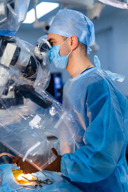 긴급 작업. 수술실에 서서 수술 중 마취 상태에서 환자를 봉합할 준비를 하는 동안 특수 장비를 보고 있는 젊은 자신감 있는 의사