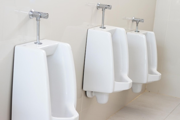 Urinals in a public restroom with one of them showing the water faucets.