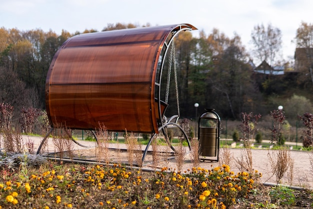 A urn in a natural park a metal bin on an openwater lawn near a\
road made of rocks in the afternoon in sunny weather swing\
garden