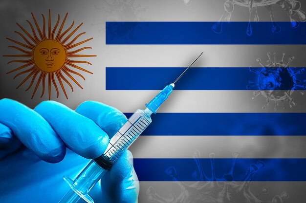 Uruguay Covid19 Vaccinatiecampagne Hand in een blauwe rubberen handschoen houdt de spuit voor de vlag