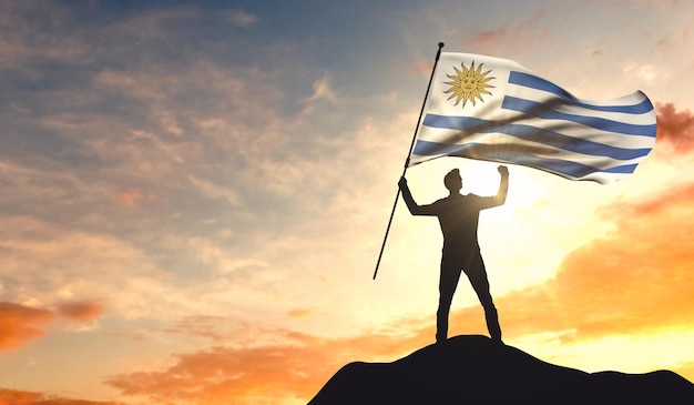 Uruguay flag being waved by a man celebrating success at the top of a mountain 3D Rendering