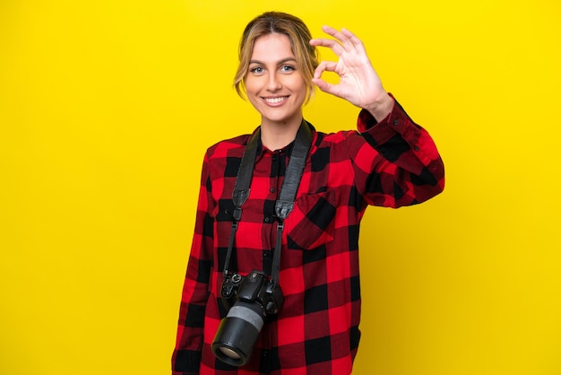 Uruguayaanse fotograafvrouw die op gele achtergrond wordt geïsoleerd die ok teken met vingers toont