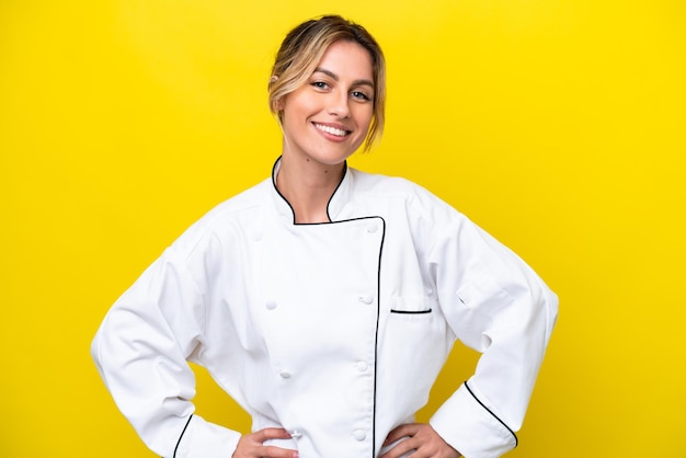 Uruguayan chef woman isolated on yellow background posing with arms at hip and smiling