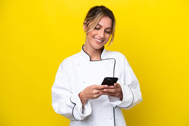 Uruguayan chef woman isolated on yellow background sending a message with the mobile