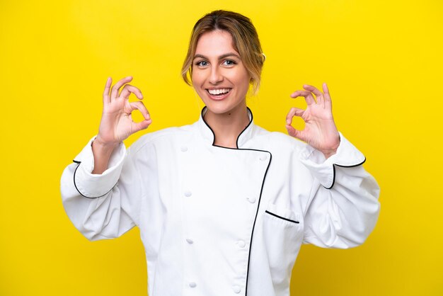 Uruguayan chef woman isolated on yellow background showing an ok sign with fingers