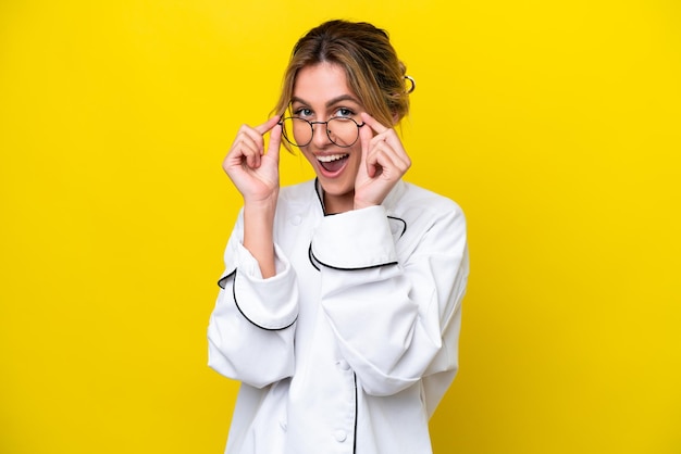 Uruguayan chef woman isolated on yellow background with glasses and surprised