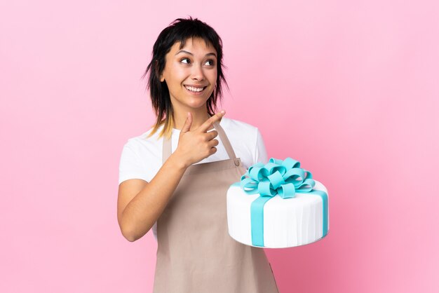 Uruguayan Pastry chef holding a big cake over isolated pink background pointing with the index finger a great idea