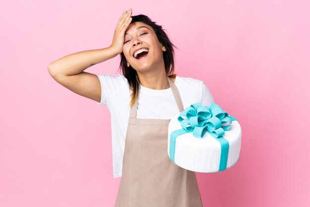 Uruguayan Pastry chef holding a big cake over pink wall laughing