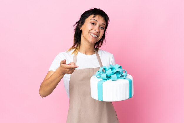 Uruguayan Pastry chef holding a big cake over pink wall points finger at you