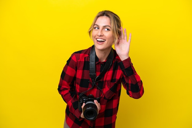 Уругвайская женщина-фотограф на желтом фоне слушает что-то, положив руку на ухо