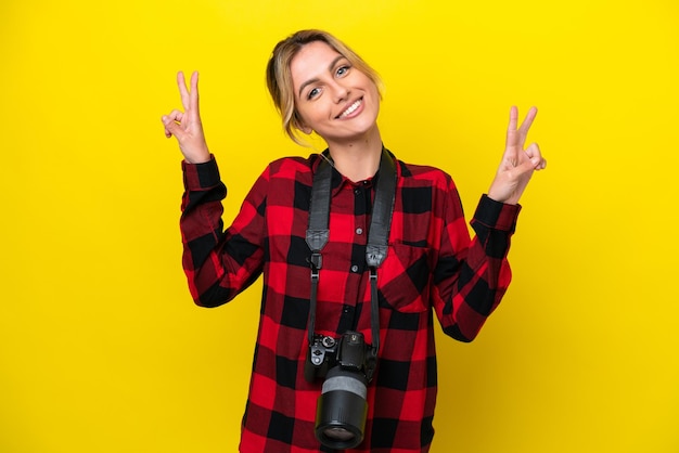 Uruguayan photographer woman isolated on yellow background showing victory sign with both hands