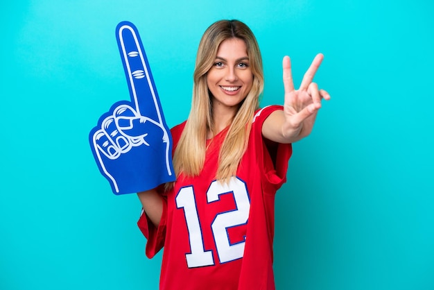 Uruguayan sports fan woman isolated on blue background smiling\
and showing victory sign
