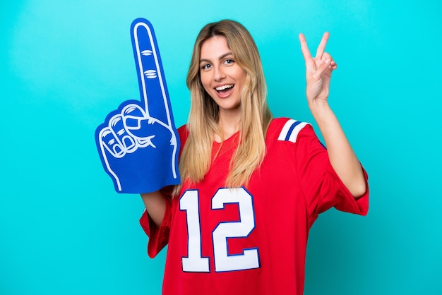 Uruguayan sports fan woman isolated on blue background smiling and showing victory sign