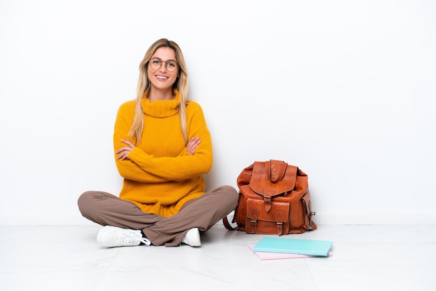 Uruguayan student woman sitting one the floor isolated on white background keeping the arms crossed in frontal position