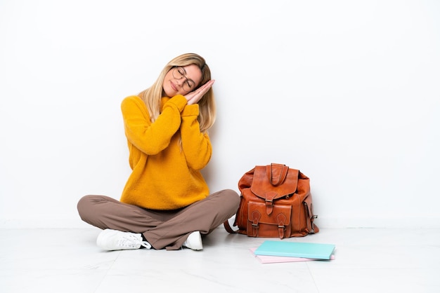 Uruguayan student woman sitting one the floor isolated on white background making sleep gesture in dorable expression