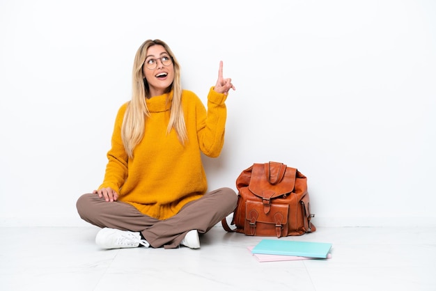 Foto studente uruguaiano donna seduta uno sul pavimento isolato su sfondo bianco rivolto verso l'alto e sorpreso