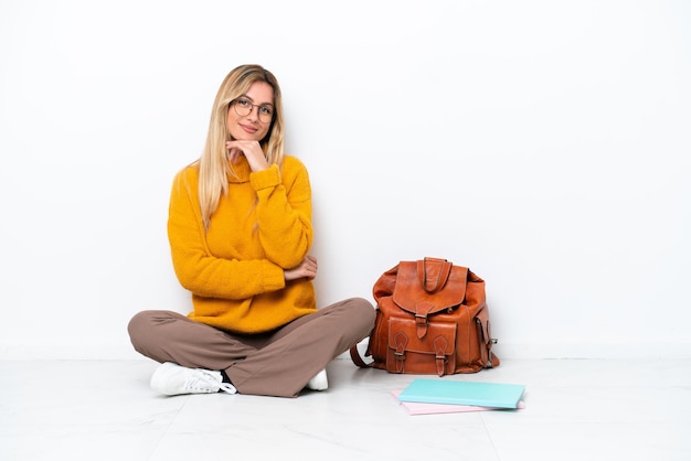 Uruguayan student woman sitting one the floor isolated on white background with glasses and smiling