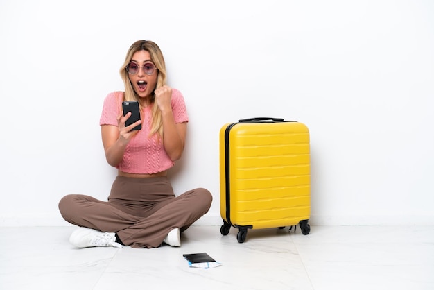 Uruguayan traveler woman sitting on the floor isolated on white background surprised and sending a message