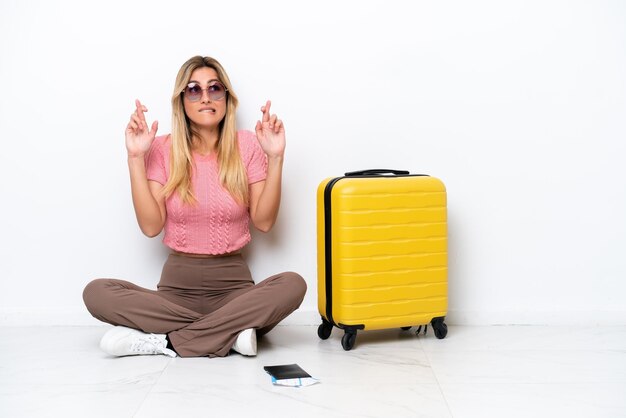 Uruguayan traveler woman sitting on the floor isolated on white background with fingers crossing