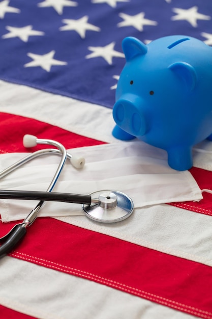Photo us of america health budget medical stethoscope protective mask and piggy bank on a usa flag closeup view