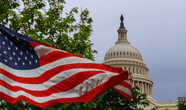 The us capitol building with a waving american flag superimposed on the sky