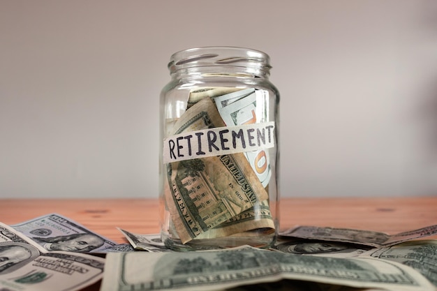 US Dollar bills in a glass jar labeled "retirement"
