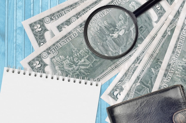 US dollars bills and magnifying glass with black purse and notepad