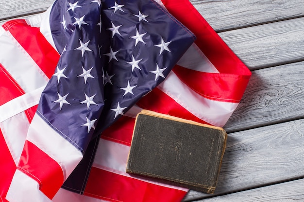 US flag beside old book. Book laying on national flag. Constitution of United States. Strict laws guarantee safety.