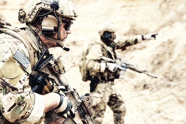 US special operations forces fighters armed with assault rifle, in opscore helmet, radio tactical ops headset, moving forward with caution in desert. Reconnaissance by fire in zone of war conflict