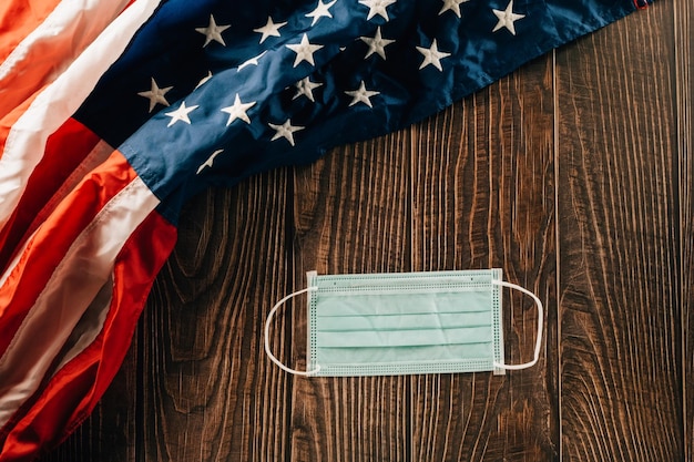 Above USA flag and face protection for coronavirus on brown old wooden background board