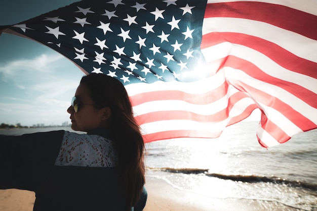 Festa dell'indipendenza usa, 4 luglio. donna che tiene la bandiera degli stati uniti d'america sulla spiaggia.