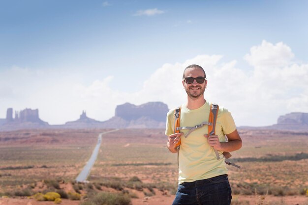 USA, Utah, portrait of smiling man with backpack and sunglasses on road to Monument Valley