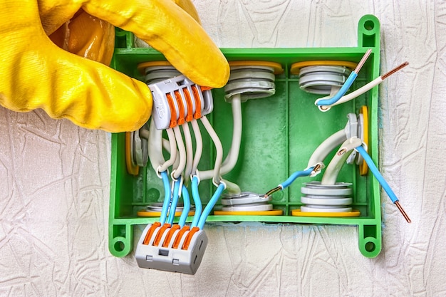 Use of a connector with a spring lever clamp for splicing conductors inside a square junction box made of green plastic. Connection of electrical wires inside terminal block. Electric installation.