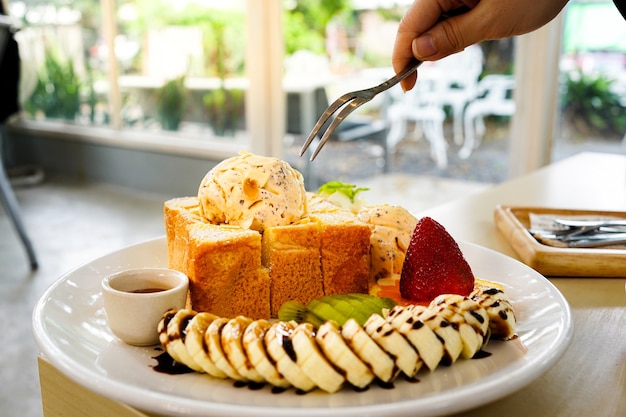 Use fork to eat honey toast bread served with mixed fruits, sliced banana, ice-cream