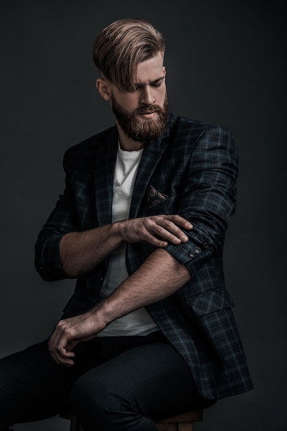 Used to look perfect. Stylishly dressed young man adjusting his jacket while sitting against grey background